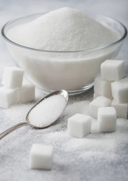 Glass bowl of natural white refined sugar with cubes and silver spoon on light table background. Space for text — Stock Photo, Image