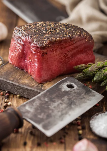 Skiva rått nötkött ovansida fog med salt och peppar på trä hackbräda med kött yxa, vitlök och sparris tips. — Stockfoto