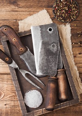 Ahşap kutuda et için eski baltalar, ahşap masa arkasında tuz ve biber, keten havlu, çatal ve bıçak. Üst görünüm
