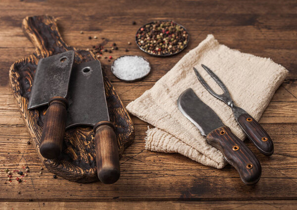 Vintage hatchets for meat on wooden chopping board with salt and pepper on wooden table background with linen towel and fork and knife.