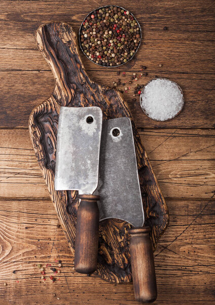 Vintage hatchets for meat on wooden chopping board with salt and pepper on wooden table background. 