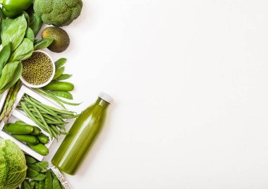 Beyaz arka planda çeşitli yeşil renkli çiğ organik sebzeler. Avokado, lahana, karnabahar ve süslemeli salatalık ve fasulye gevşek biber ve bir şişe smoothie. Metnin için boşluk