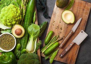 Koyu arka planda ahşap kutuda çeşitli yeşil tonlu ham organik sebzeler. Avokado, lahana, karnabahar ve salatalık ile kesilmiş fasulye ve Doğrama tahtası ile bıçak.