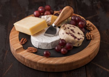 Tahtada çeşitli peynirler ve ahşap zeminde üzümler. Mavi Stilton, Kırmızı Leicester ve Brie Cheese ve fındık.