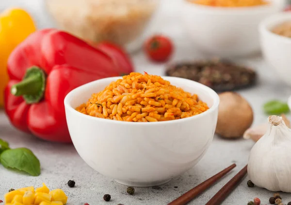 White ceramic bowl plate with boiled red long grain basmati rice with vegetables on light table background with sticks and paprika pepper with corn,garlic and basil. Top view — Stock Photo, Image
