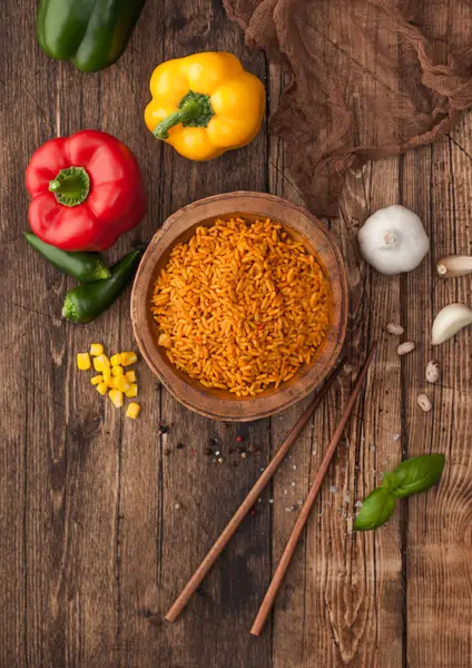 Wooden bowl with boiled red long grain basmati rice with vegetables on wooden table background with sticks and paprika pepper with corn,garlic and basil. Top view — Stock Photo, Image