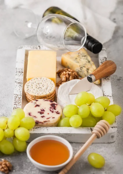 Glas und Flasche Weißwein mit verschiedenen Käsesorten in Holzkiste und Trauben auf Holztischhintergrund. Blue Stelton, Roter Leicester und Brie-Käse und Cheddar mit Nüssen und Honig. — Stockfoto