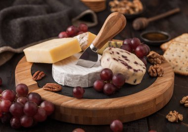 Tahtada çeşitli peynirler ve ahşap zeminde üzümler. Mavi Stilton, Kırmızı Leicester ve Brie Cheese ve fındık kraker ve bal.