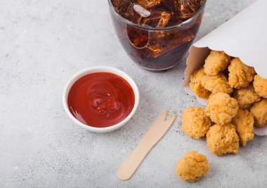 Hafif arka planda ketçap ve kola bardağı ile fast food yemek için beyaz kağıt kapta Gevrek güney tavuk patlamış mısır ısırıkları. 