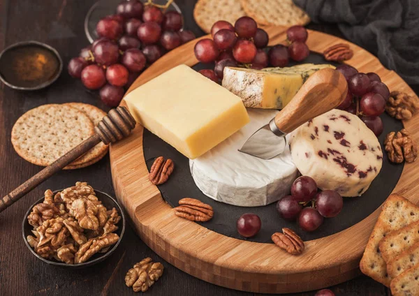Tahtada çeşitli peynirler ve ahşap zeminde üzümler. Mavi Stilton, Kırmızı Leicester, Brie Cheese, kraker ve ballı fındık. Üst görünüm.