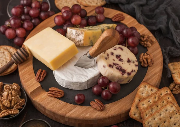 Tahtada çeşitli peynirler ve ahşap zeminde üzümler. Mavi Stilton, Kırmızı Leicester, Brie Cheese, kraker ve ballı fındık. Üst görünüm.