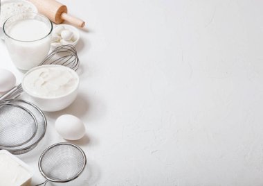 Beyaz masa arka planda taze süt ürünleri. Süt, un kase, ekşi krema ve süzme peynir ve yumurta bardak. Çelik çırpMa teli ve oklava. Üst te. Metin için alan