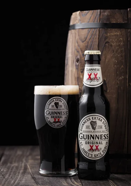London, UK - 27 april 2018: Fles en origineel glas Guinness extra stout bier naast oud houten vat. — Stockfoto