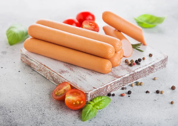Classic boiled meat pork sausages on chopping board with pepper and basil and cherry tomatoes on light background. — Stock Photo, Image