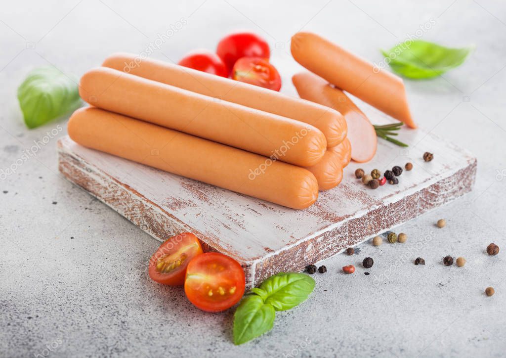 Classic boiled meat pork sausages on chopping board with pepper and basil and cherry tomatoes on light background.