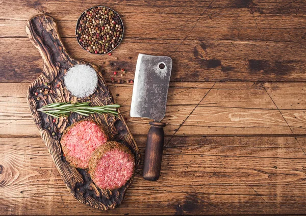 Burgers de bœuf au poivre haché cru frais sur planche à découper vintage avec épices et herbes et hachette de viande sur fond en bois . — Photo
