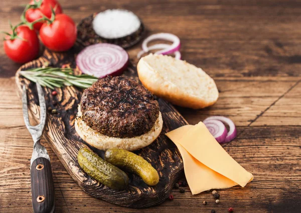 Hamburguesa de carne fresca de pimiento picado a la parrilla sobre tabla de cortar vintage con bollos de cebolla y tomates sobre fondo de madera. Vista superior —  Fotos de Stock