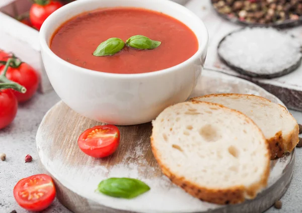 白碗一盘奶油西红柿汤，汤匙放在轻薄的桌子上，背景上有一盒生西红柿和面包. — 图库照片