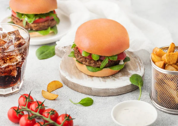 Healthy vegetarian meat free burgers on round chopping board with vegetables on light table background with potato wedges and glass of cola. Top view. — Stock Photo, Image