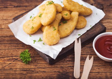 Ahşap arka plan üzerinde ahşap çatal ve ketçap ile doğrama tahtası üzerinde tereyağlı tavuk nuggets.