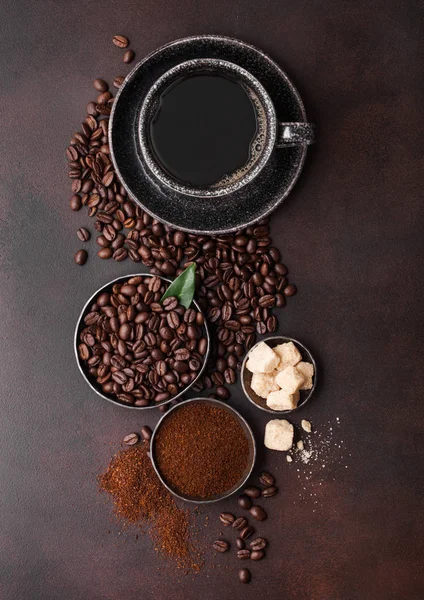 Cup of fresh raw organic coffee with beans and ground powder with cane sugar cubes with coffee tree leaf on brown background. — Stock Photo, Image