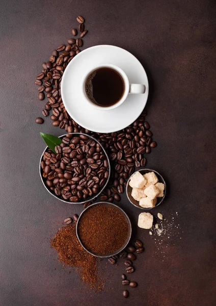 White cup of fresh raw organic coffee with beans and ground powder with cane sugar cubes with coffee tree leaf on brown background. Top view — 스톡 사진