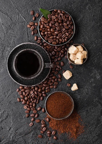 Cup of fresh raw organic coffee with beans and ground powder with cane sugar cubes with coffee tree leaf on black background. Top view — Stock Photo, Image