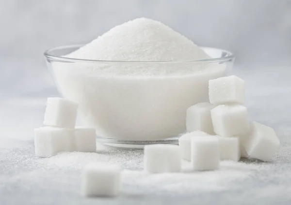 Glass bowl of natural white refined sugar with cubes on light table background. — Stock Photo, Image