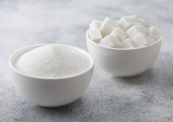 White bowl plates of natural white sugar cubes and refined sugar on light table background.