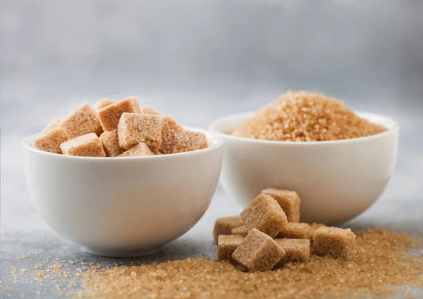 White bowl plates of natural brown sugar cubes and refined sugar on light table background. — Stock Photo, Image