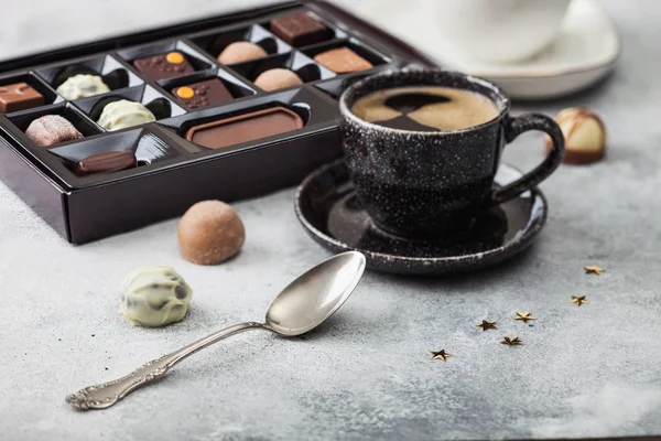 Коробка роскошных шоколадных конфет с чашкой черного кофе и серебряной ложкой на светлом фоне стола . — стоковое фото