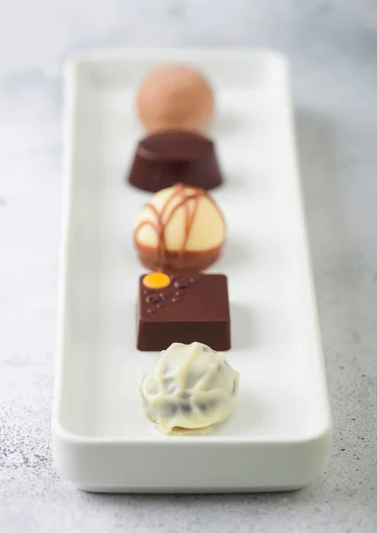 Selección de caramelos de chocolate de lujo en placa de porcelana blanca sobre fondo de mesa claro. Surtido de chocolate blanco, oscuro y leche . — Foto de Stock