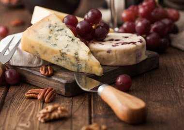 Tahtada çeşitli peynirler ve ahşap zeminde üzümler. Mavi Stilton, Kırmızı Leicester ve Brie Cheese ve fındık.