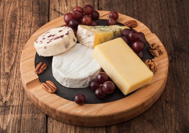 Tahtada çeşitli peynirler ve ahşap zeminde üzümler. Mavi Stilton, Kırmızı Leicester ve Brie Cheese ve fındık.