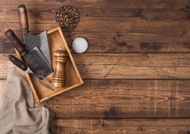 Ahşap kutuda et, ahşap masa arkasında tuz ve biber ve keten havlu ve çatalla birlikte antika baltalar. Üst görünüm