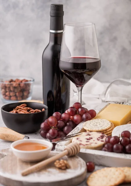 Fles en glas rode wijn met een selectie van verschillende kaas in houten doos en druiven op lichte tafel achtergrond. Blue Stilton, Red Leicester en Brie Cheese met Cheddar en noten met honing. — Stockfoto