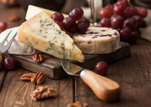 Tahtada çeşitli peynirler ve ahşap zeminde üzümler. Mavi Stilton, Kırmızı Leicester ve Brie Cheese ve fındık. — Stok fotoğraf