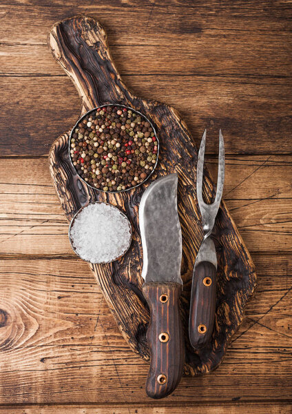 Vintage fork and knife for meat on wooden chopping board with salt and pepper on wooden table background. 