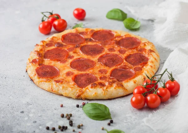 Fresh round baked Pepperoni italian pizza with tomatoes with basil on ligh background with linen towel.