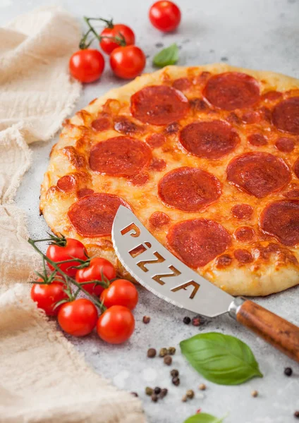 Fresh round baked Pepperoni italian pizza with knife with tomatoes and basil on light background with linen towel. Top view