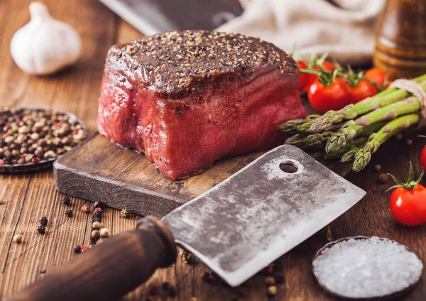 Skiva rått nötkött ovansida fog med salt och peppar på trä hackbräda med kött yxa, vitlök och sparris tips. — Stockfoto