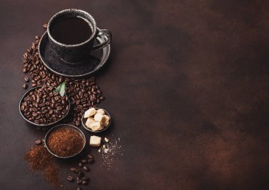 Fasulyeli taze çiğ organik kahve ve koyu arkaplanda kahve ağacı yaprağı olan şeker küplü öğütülmüş toz. Siyah seramik bardak