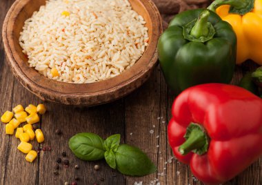Ahşap kase, haşlanmış uzun tahıllı basmati pilavı, ahşap masa arkasında sebzeli, biberli, mısır ve fesleğenli.. 