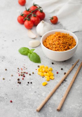 Beyaz seramik kâse tabağı, haşlanmış kırmızı uzun taneli basmati pilavı, hafif arka planda sebzeler, çubuklar, mısır, sarımsak ve fesleğenli domatesler.. 