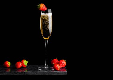 Zarif bir bardak sarı şampanya üzerinde çilek ve siyah mermer tahtada taze böğürtlen..
