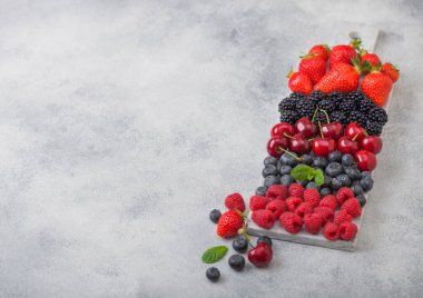 Açık mutfak arka planında beyaz mermer tahtada taze organik böğürtlen karışımı. Ahududu, çilek, yabanmersini, böğürtlen ve kiraz. Üst görünüm