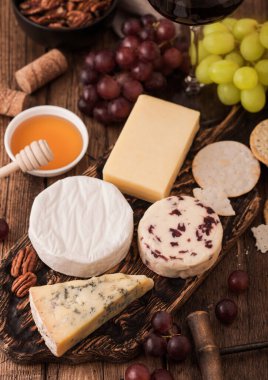 Tahtada çeşitli peynirler ve ahşap masa arkasında üzümler. Mavi Stilton, Kırmızı Leicester ve Brie Cheese.