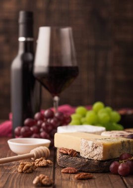 Tahtasında çeşitli peynir ve ahşap masa zemininde üzümler bulunan bir şişe kırmızı şarap. Mavi Stilton, Kırmızı Leicester ve Brie Cheese ve bıçak.