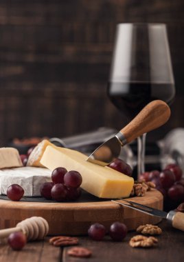Tahtasında çeşitli peynirler ve ahşap masa zemininde üzümler olan bir bardak kırmızı şarap. Mavi Stilton, Kırmızı Leicester ve Brie Cheese ve bıçaklı ballı.