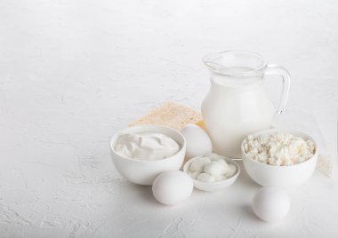 Beyaz masa arka planında taze süt ürünleri. Bir kavanoz süt, bir kase ekşi krema, süzme peynir ve mozzarella. Yumurta ve peynir.. 